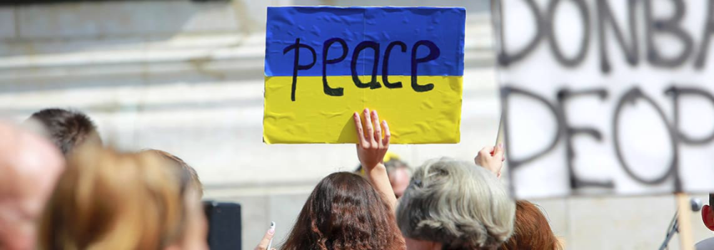 Nainen pitää kädessä ukrainan lippua, jossa teksti peace