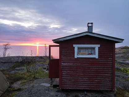 Kuvassa saunamökki pienessä saaressa. Auringonlasku.