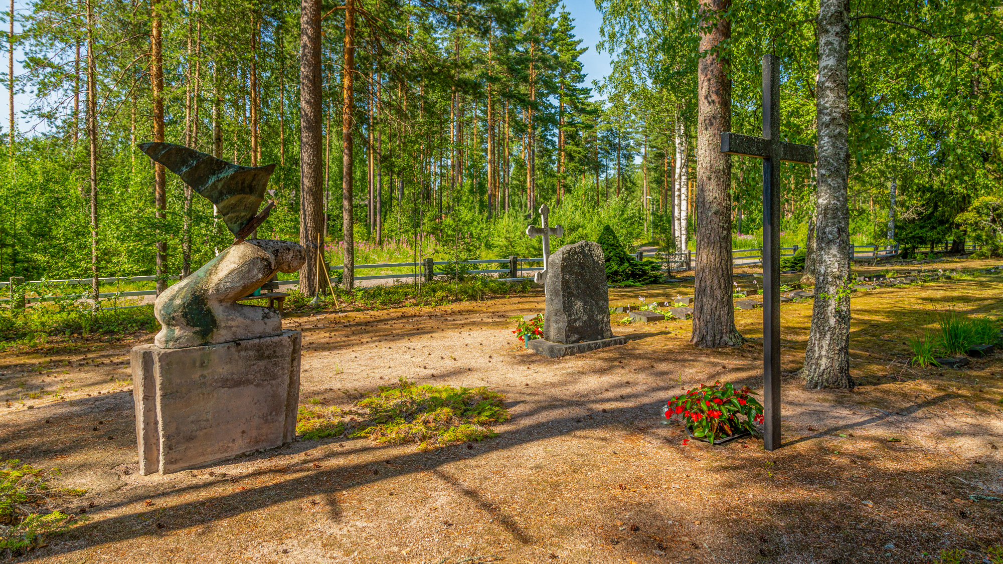 Kesäinen näkymä Rauhan hautausmaalle. Vasemmalla enkeliveistos keskellä muistomerkki ja oikealla risti.