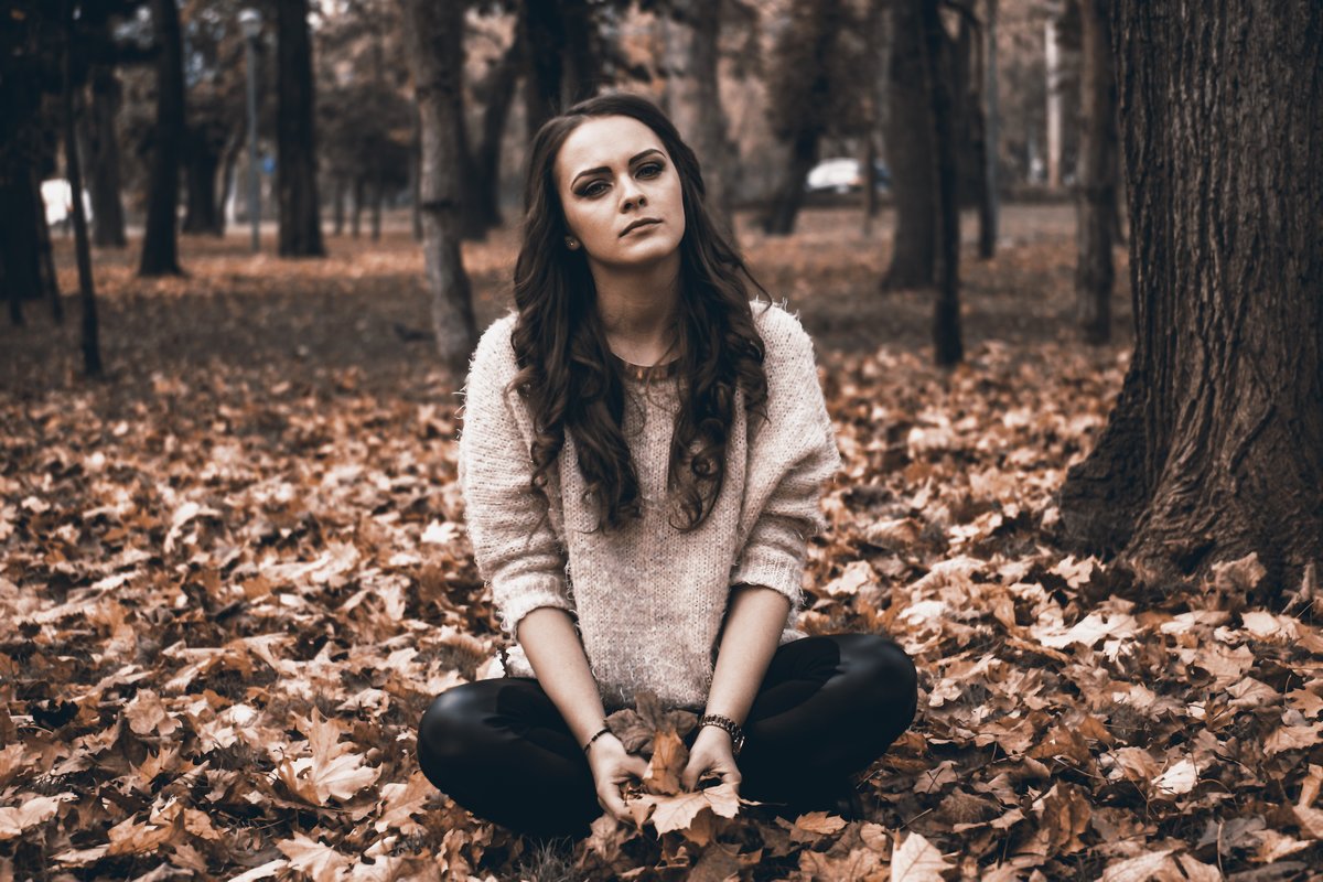 Tyttö istuu yksin syksyisessä metsässä