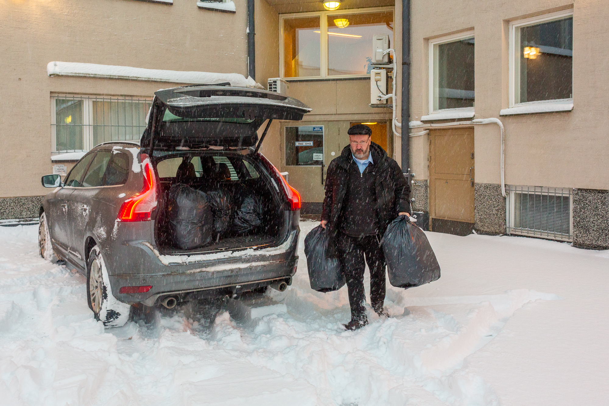 Timo Rosqvist kantaa neulesäkkejä autoon lumisella pihalla.